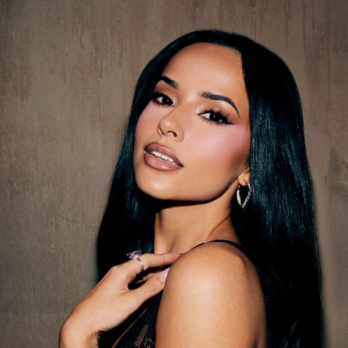 Retrato de Becky G posando frente a una pared texturizada, con maquillaje definido y un outfit negro de encaje, en una composición de estilo editorial.