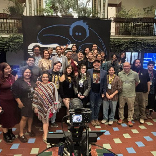 Fotografía grupal de asistentes a un evento académico sobre videojuegos frente a un fondo institucional.