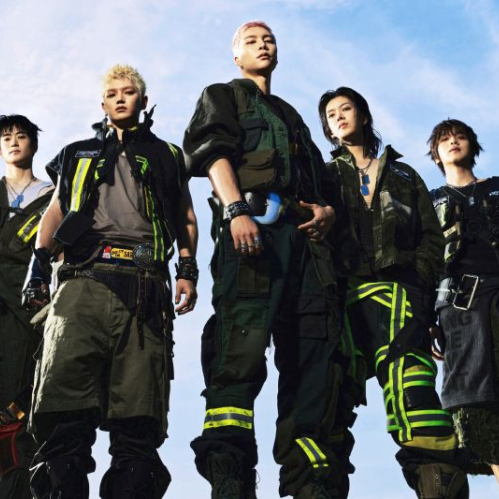Fotografía promocional de los integrantes de la agrupación de K-pop NCT 127. Aparecen cinco miembros posando en contrapicado bajo un cielo azul despejado, luciendo atuendos de estilo industrial y táctico en tonos verde oliva, negro y beige con cintas fluorescentes.