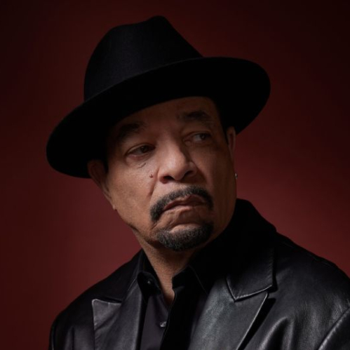 Retrato de un hombre con sombrero y chaqueta oscura sentado frente a un fondo rojo, en un ambiente de iluminación dramática.