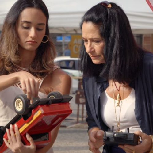 Dos personas observan un objeto mientras manipulan un control remoto en un entorno urbano bajo una carpa.