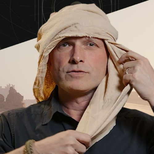 Fotografía del instructor de supervivencia militar John Hudson ajustándose un turbante o paño tradicional de desierto, con paisajes de formaciones rocosas de Arrakis al fondo.  