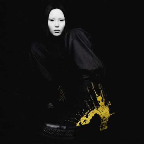 Persona vestida de negro en un entorno oscuro, con botas negras intervenidas con pintura amarilla que destacan por su contraste visual.
