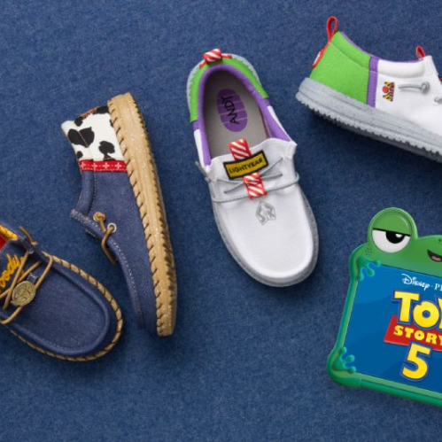Fotografía de producto en vista superior cenital con cuatro modelos de calzado mocasín de la colaboración HEYDUDE x Toy Story, dispuestos sobre un fondo textil azul de mezclilla junto al logotipo oficial de la película en forma de juguete de rana verde.