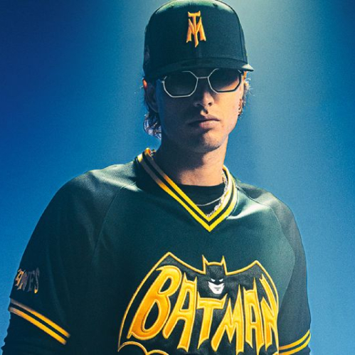Persona con jersey y gorra inspirados en Batman, iluminado con tonos azules en un entorno oscuro.