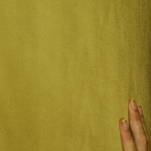 Persona apoyada contra una pared amarilla en un entorno inquietante, evocando tensión y atmósfera claustrofóbica.