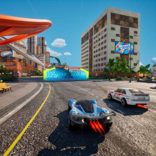Captura de pantalla de la jugabilidad del videojuego "HOT WHEELS Infinite Rush" en la isla Wheelswood. En primer plano, en una carretera de asfalto gris, se aprecian dos vehículos a escala compitiendo: a la izquierda, un superdeportivo azul futurista con luces traseras en forma de propulsor naranja encendidas, y a la derecha, un vehículo clásico deportivo de color blanco con franjas rojas. En el fondo, se erige un rascacielos de estilo residencial junto a palmeras y una montaña rocosa bajo un cielo azul despejado con nubes delgadas y un globo aerostático. A la izquierda, una pista naranja icónica de Hot Wheels se extiende por encima de la acera, y en la esquina inferior izquierda se observa el logotipo oficial de "HOT WHEELS Infinite Rush".
