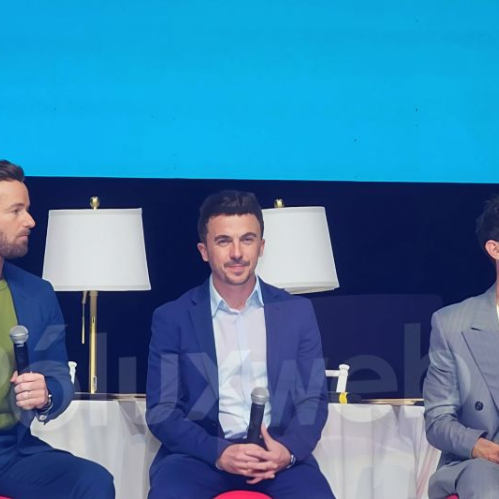 Tres integrantes del elenco de Malcolm in the Middle sentados en un panel durante un evento en Ciudad de México. Cada uno sostiene un micrófono mientras conversan frente a un fondo azul, con dos lámparas blancas colocadas detrás de ellos.
