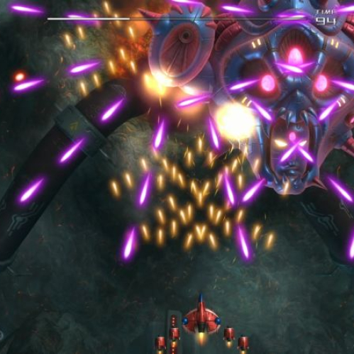 Captura de pantalla de la jugabilidad del videojuego de disparos "Truxton Extreme" durante el Nivel 1. En el centro de la pantalla, una gigantesca nave nodriza alienígena o jefe con forma de rostro robótico biomecánico y ojos brillantes de color amarillo y rosa dispara una ráfaga masiva de proyectiles láser de color morado y naranja en un patrón de abanico. En la parte inferior, una pequeña nave de combate del jugador de color rojo y azul esquiva los ataques mientras dispara hacia arriba. El fondo es un entorno orgánico oscuro y rocoso. En la esquina superior izquierda se muestran los marcadores de puntaje ("SCORE 1 967 270") y lives, mientras que en la esquina inferior izquierda se ven iconos de bombas de energía.