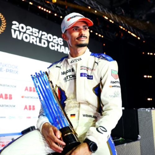 Fotografía del piloto Pascal Wehrlein vistiendo su uniforme de careras blanco y azul con gorra mientras sostiene el trofeo del campeonato mundial frente a un fondo del evento.
