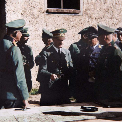 Grupo de oficiales militares reunidos alrededor de un mapa en un entorno exterior.