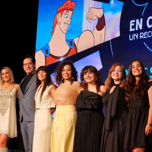 Siete integrantes del elenco y producción posan frente a una pantalla con arte promocional del concierto.