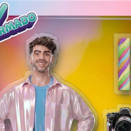 Imagen promocional oficial de confirmación para "La Casa de los Famosos México". Al centro aparece Fede Vigevani, un joven de tez clara con cabello castaño corto y ondulado, sonriendo a la cámara y vistiendo una playera azul bajo una camisa o chamarra rosa brillante con acabado metálico o iridiscente. En la esquina superior izquierda destaca un logotipo con la palabra "CONFIRMADO" en letras verdes dentro de un contorno blanco y con un icono de palomita. A la derecha del personaje, flotando sobre un fondo degradado entre tonos cálidos de amarillo y rosa, se aprecian recortes en el empaque que muestran un dulce cilíndrico multicolor y una cámara fotográfica profesional de color negro.