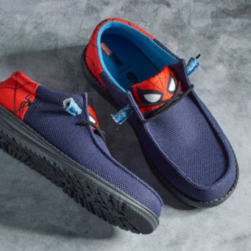 Fotografía de producto en vista superior de un par de calzado mocasín casual modelo Wally Funk en azul marino, con paneles traseros y lengüeta en rojo decorados con el diseño de la máscara y telarañas de Spider-Man sobre una superficie gris de concreto.