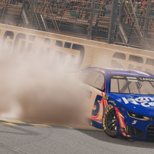 Captura de pantalla directa del videojuego NASCAR 26 que muestra una dramática maniobra de derrape o burnout sobre el asfalto. En el centro de la toma destaca un auto de carreras Chevrolet Camaro en color azul brillante con detalles en blanco y rojo, marcado con el número 5 y el patrocinador HendrickCars.com. En la parte superior del parabrisas se observa el apellido del piloto Larson. Detrás del vehículo se genera una densa nube de humo blanco y polvo que cubre la barda de contención del circuito Chicagoland Speedway, con las gradas llenas de espectadores al fondo.