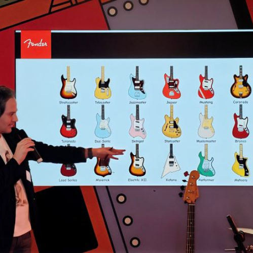 Presentador frente a una pantalla que muestra ilustraciones de modelos de guitarra Fender durante una sesión informativa.