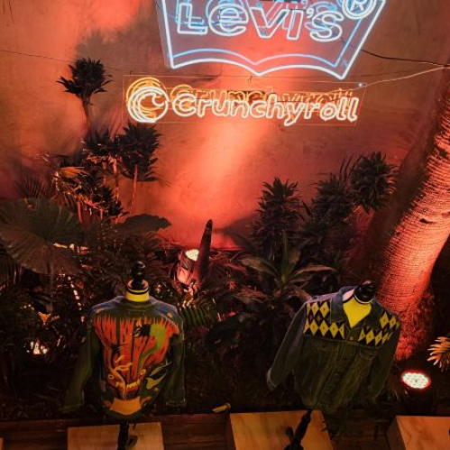Exhibición de chamarras intervenidas por artistas mexicanos en un espacio iluminado con neón y ambientación tropical.