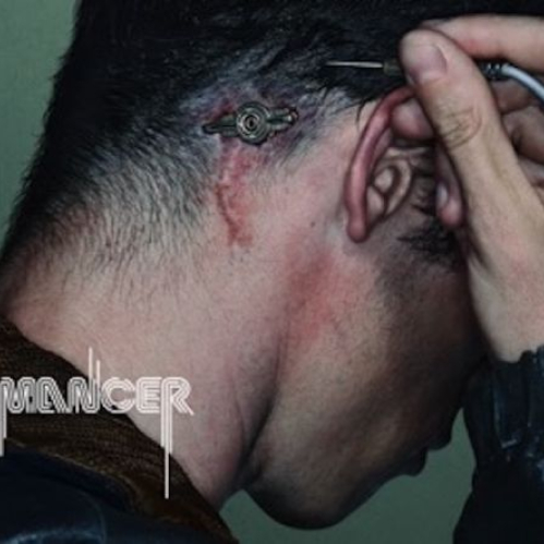 Fotografía de plano corto en perfil de la nuca y cabeza de un hombre con cabello oscuro corto. Detrás de su oreja se aprecia un implante cibernético metálico circular insertado en la piel con marcas de cicatriz y una pequeña incisión ensangrentada, mientras la mano sostiene una clavija conectada al puerto. En la esquina inferior izquierda aparece el logotipo oficial de "Neuromancer" y en la inferior derecha el isotipo de Apple TV.