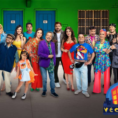 Elenco reunido frente a un edificio verde con puertas azules, posando en un ambiente colorido que refleja el tono humorístico de la serie.
