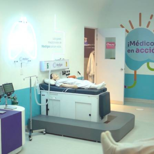 Sala educativa con una cama hospitalaria, un maniquí médico y proyecciones luminosas que explican funciones del cuerpo humano en un entorno interactivo.