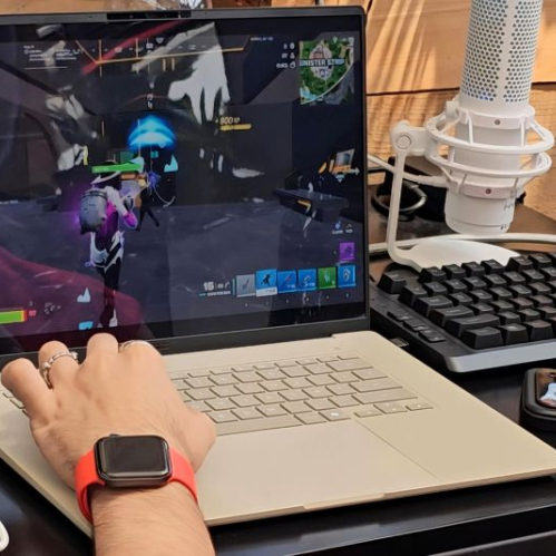 Fotografía en primer plano de un jugador utilizando una laptop impulsada por Snapdragon X durante el Bootcamp. En la pantalla se observa el videojuego Fortnite en plena partida mientras el jugador interactúa con el teclado y cuenta con un micrófono de estudio HyperX a un costado.