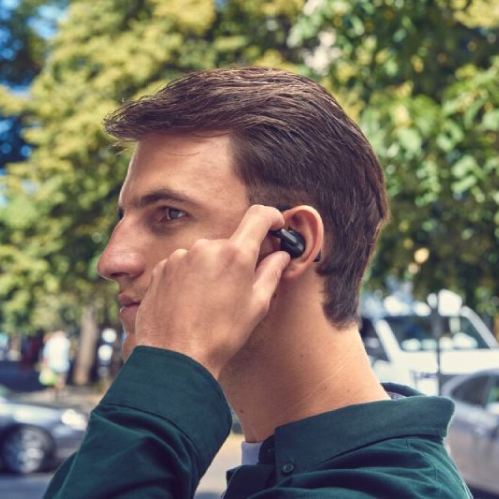 Perfil de un hombre joven caminando en la calle utilizando los audífonos inalámbricos de oído abierto JBL Sense Pro de color negro ajustados sobre su oreja.