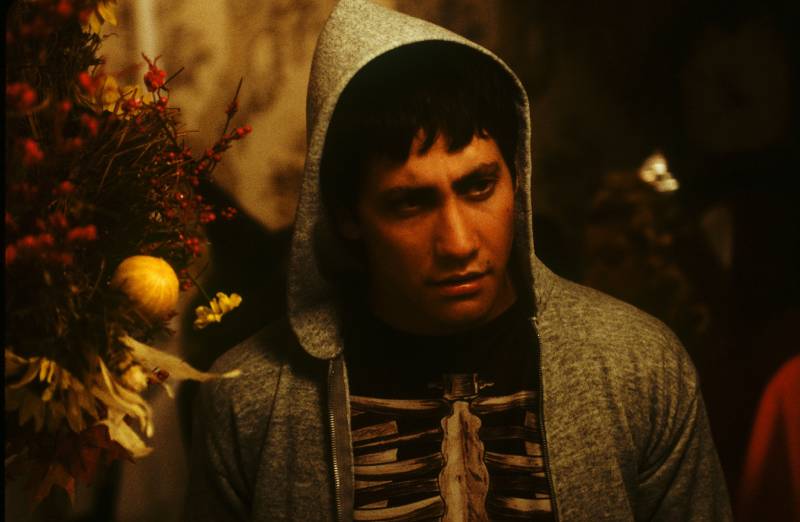 Persona con sudadera gris y camiseta oscura, observando hacia abajo en un ambiente interior tenue con elementos decorativos cálidos.