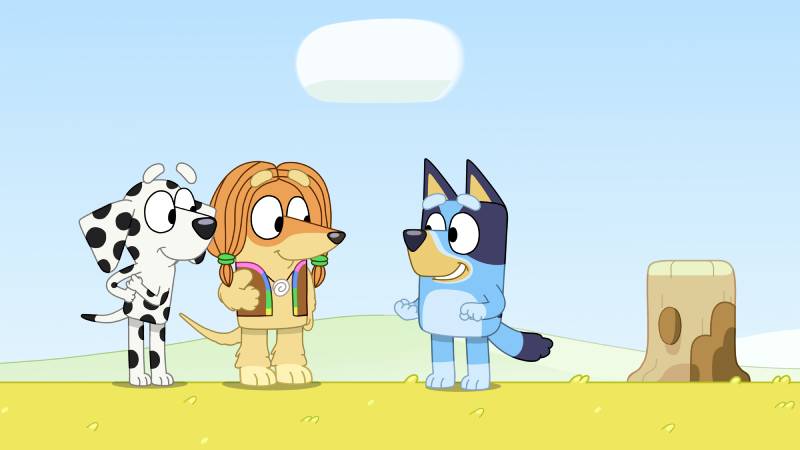 Bluey — Momentos de Diversión con Amigos Tres personajes caninos animados conversan en un campo verde bajo un cielo despejado, transmitiendo un ambiente amistoso y alegre.