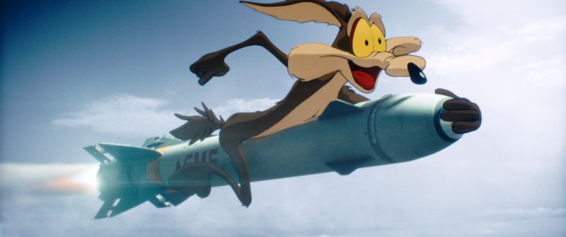 El Coyote sobre un cohete ACME en Coyote vs Acme El personaje animado del Coyote aparece montado sobre un cohete espacial azul con el logotipo de la marca ACME mientras surca un cielo azul con nubes dispersas.