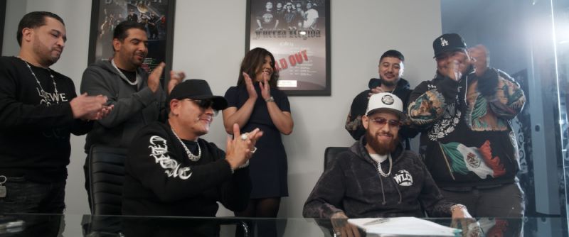 Firma de contrato – Clika Grupo celebrando la firma de un documento en una oficina con pósters en la pared.