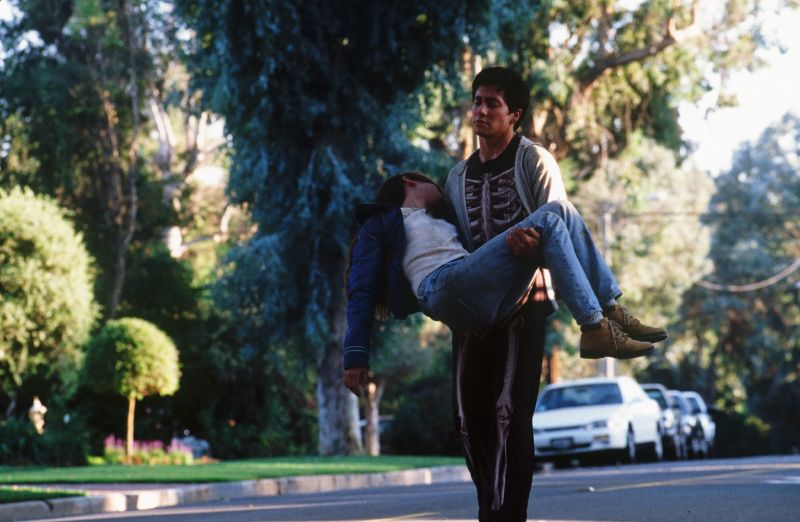 Escena dramática en suburbio – Donnie Darko Persona cargando a otra en una calle suburbana, en un momento dramático y emocional.