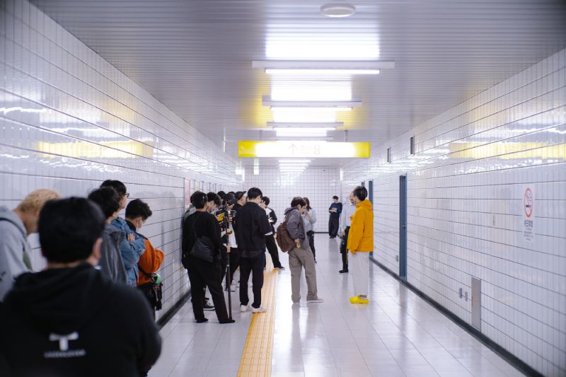 Corredor subterráneo con personas esperando y un camino táctil amarillo al centro.