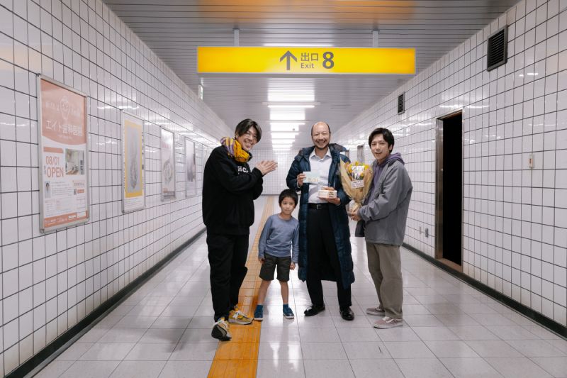Grupo de personas reunidas bajo un letrero de “Exit 8” en un pasillo subterráneo.