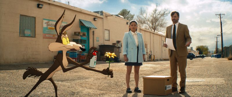 El Coyote junto a Lana Condor y Will Forte El Coyote sosteniendo una flor y una lata de spray de broma en un callejón frente a Lana Condor y Will Forte.