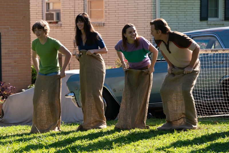 Familia protagonista en El final de la Calle Oak Escena retrospectiva o cotidiana que muestra a Anne Hathaway, Ewan McGregor y sus dos hijos riendo y compitiendo alegremente en una carrera de costales en el jardín de su casa.