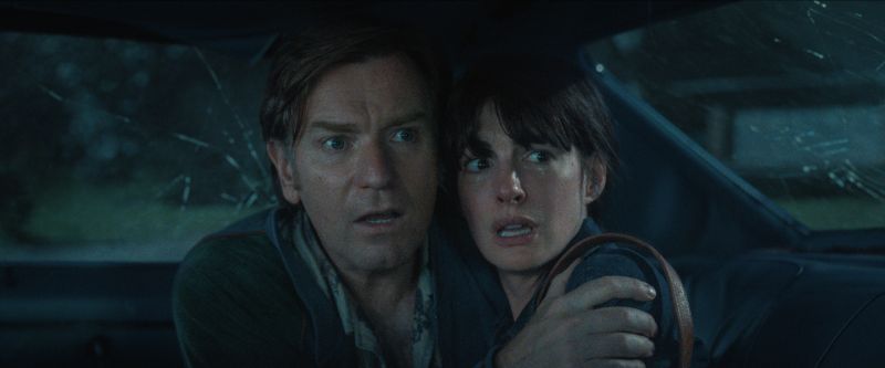 Tensión y supervivencia en El final de la Calle Oak Plano medio cerrado desde el interior de un automóvil con los cristales estrellados donde Ewan McGregor abraza con tensión a Anne Hathaway mientras ambos observan aterrados hacia el exterior.
