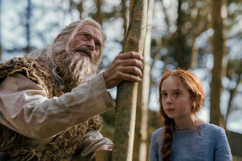 Robin Hood y Margaret en el bosque Plano medio de un anciano Robin Hood (Hugh Jackman) sosteniendo una vara de madera en el bosque mientras mira hacia arriba preocupado al lado de la joven Margaret (Faith Delaney).