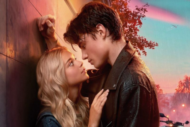 Escena romántica en Tu corazón será destrozado Plano medio corto de la pareja protagonista mirándose fijamente a los ojos a punto de besarse bajo un ambiente iluminado por tonos cálidos y fríos al atardecer.