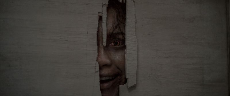 El horror acecha tras las paredes en Evil Dead: En Llamas Una entidad poseída observa a través de una abertura en una pared, anticipando uno de los momentos de mayor tensión del filme.