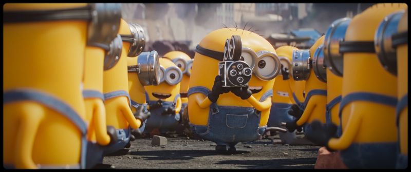 Minion filmando con una cámara antigua mientras otros observan la escena.