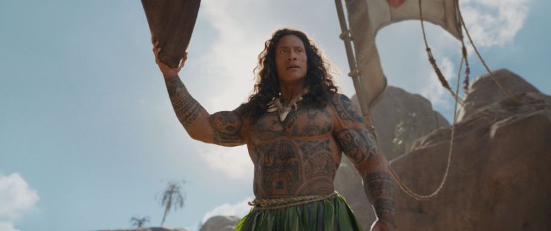 Maui — Representación en acción real Maui aparece con tatuajes polinesios y un arma ceremonial en un entorno rocoso.