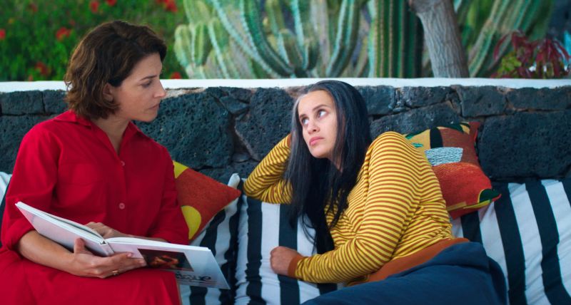 Dos personas conversando en un sofá exterior junto a cactus.