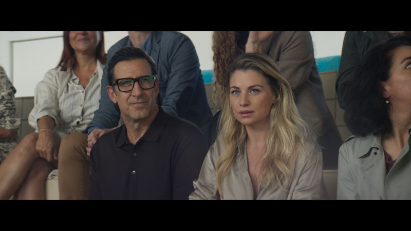 Captura de pantalla de la película Deseo que muestra a la pareja protagónica sentada en unas gradas con expresiones de preocupación y seriedad.