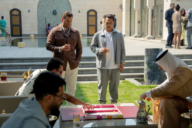 Personas reunidas en un patio elegante mientras dos juegan backgammon.