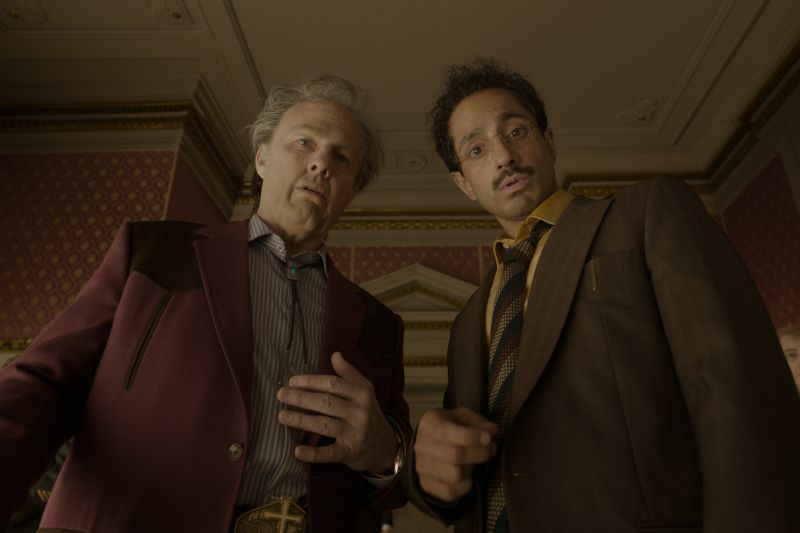 Tom Cruise y Riz Ahmed en escena de Digger Tom Cruise y Riz Ahmed observando hacia abajo en un ángulo contrapicado en el interior de una elegante habitación decorada.