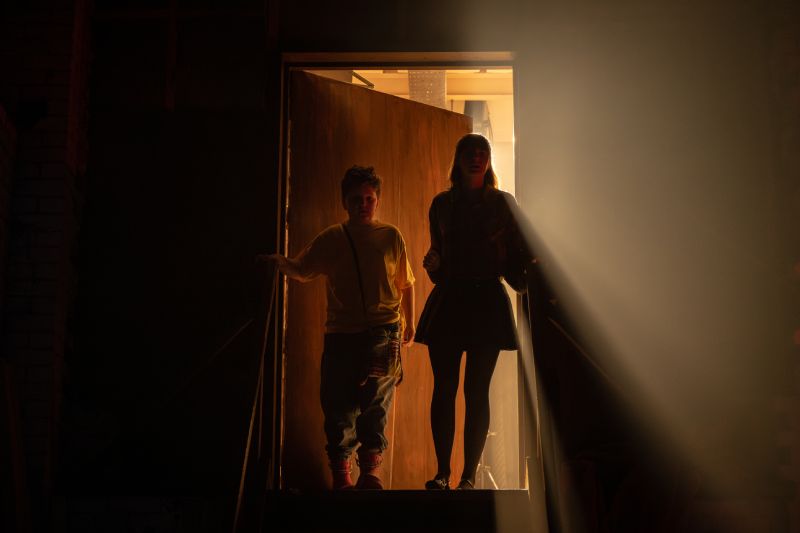Siluetas en el taller de marionetas Siluetas de dos jóvenes entrando por una puerta iluminada por un fuerte haz de luz contraluz desde el exterior.