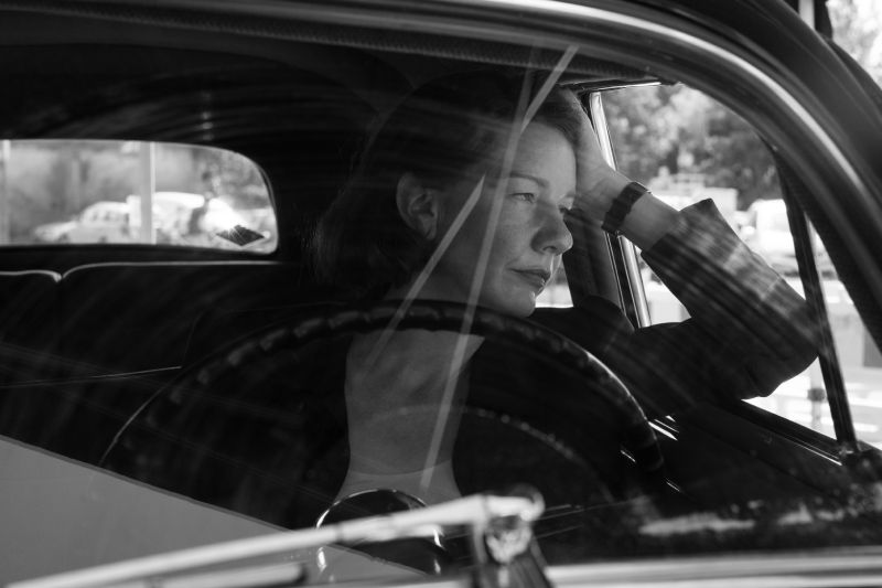 Reflexión y Melancolía en el Exilio Sandra Hüller sentada al volante de un automóvil clásico, apoyando la cabeza en su mano con una expresión de profunda reflexión y cansancio.