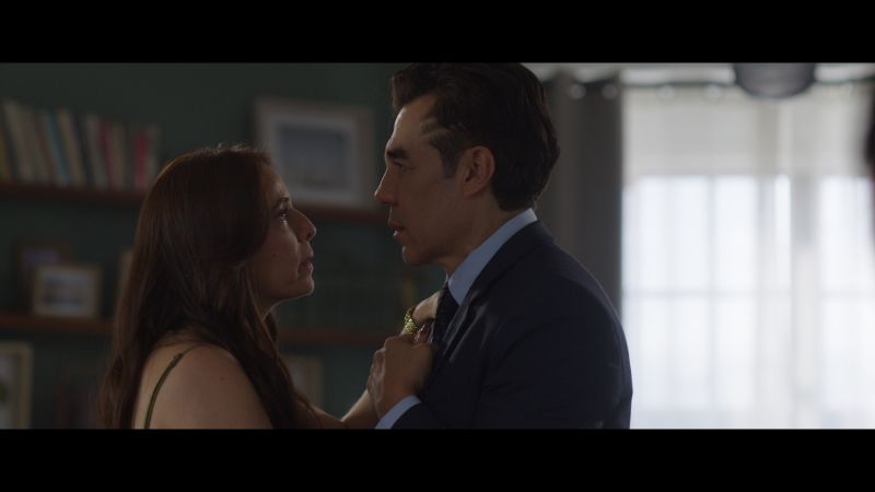 Juan Pablo y su esposa en un momento de tensión emocional Juan Pablo (Adrián Uribe) sosteniendo cariñosamente las manos de su esposa (Mónica Huarte) mientras se miran fijamente a los ojos en una escena dramática dentro de su casa.
