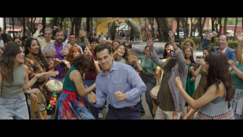 Juan Pablo bailando al aire libre en una plaza pública Juan Pablo bailando eufórico con camisa azul en medio de una multitud alegre en una plaza pública al aire libre en Coyoacán.