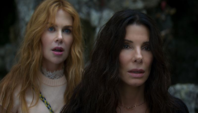 Sandra Bullock y Nicole Kidman en escena de Hechizo de amor 2 Sandra Bullock con cabello largo y oscuro en primer plano junto a Nicole Kidman pelirroja al fondo, ambas con expresiones de asombro y preocupación mirando hacia el frente.